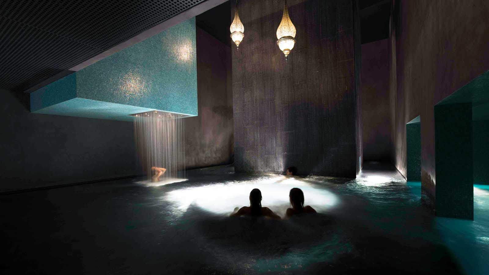 two persons in a jacuzzy and one enjoying a waterfall in the Bain Bleu spa Geneva best things to do in Geneva