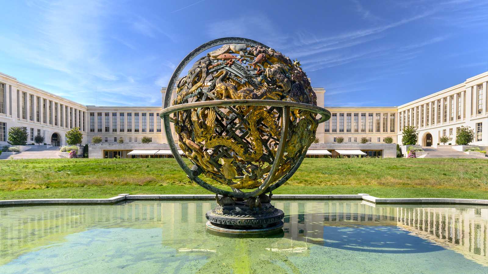  statue of the globe in a founain in front of the white building of the United Nations Palace, the UN headquarter in Geneva