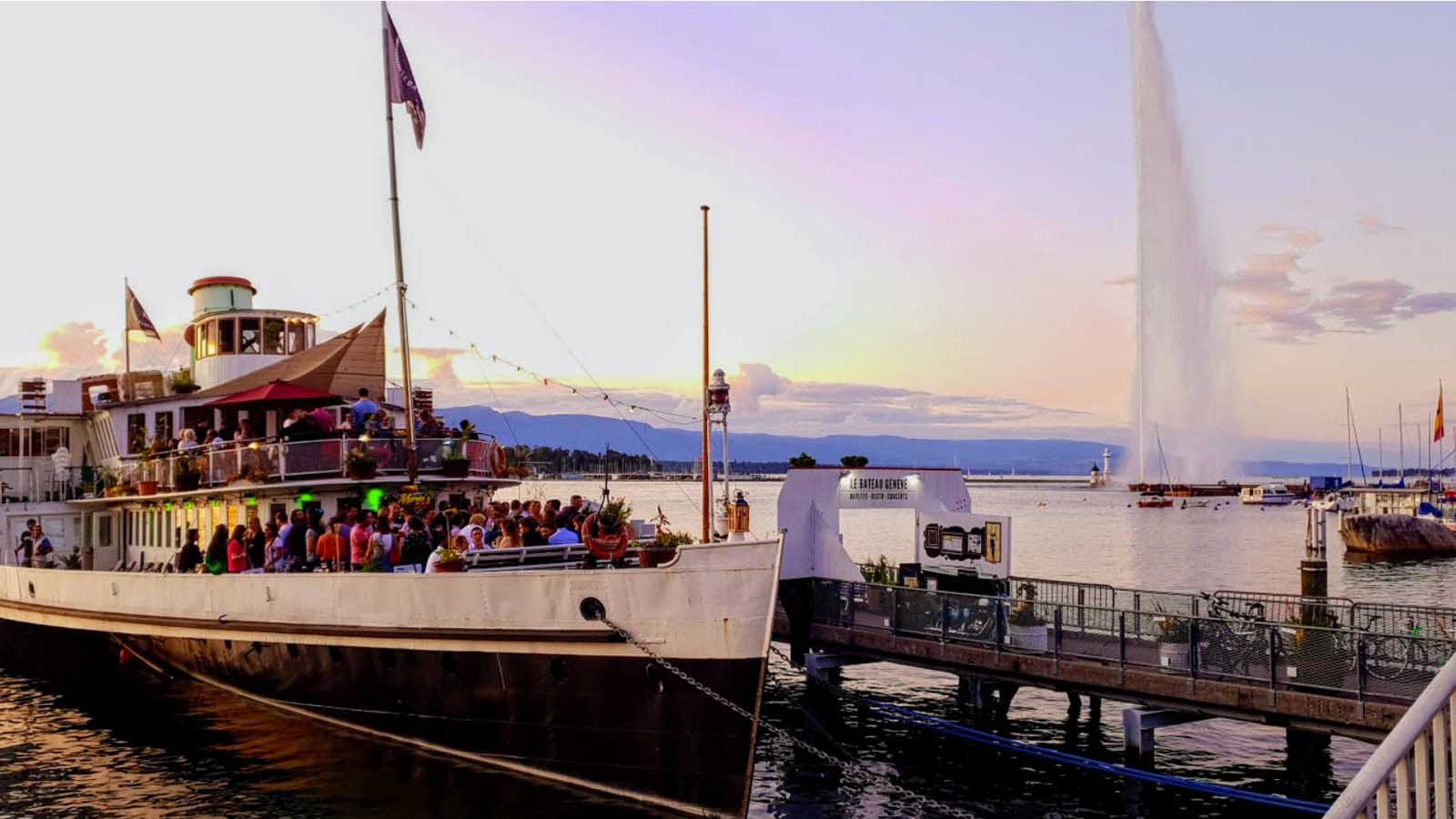 People enjoying the pink colours of the sunset on  lake Geneva with the Jet d'Eau in the background what to do in geneva
